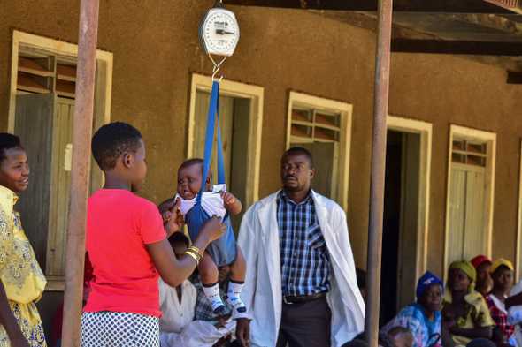A mother weighs her baby at Kibibi Health center Jinja District, as nurse Joshua Musomba watches. Infant mortality in Uganda is about 336 deaths per 100,000 live births. [Al Jazeera]