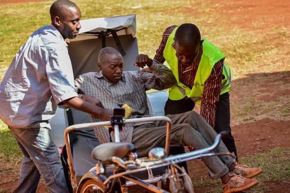 Harid Mukasa, a member of the Village Health Team with another man helps transfer a patient from the ambulance to a ward at Budondo health centre. In Uganda, fewer than 7 percent of patients arrive at health facilities by ambulance. [Nicholas Bamulanzeki/Al Jazeera]